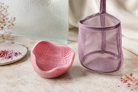 Tapis de nettoyage en silicone rose plié en bol, accompagné d’un filet de séchage suspendu.
