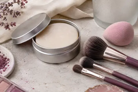 Savon solide pour pinceaux dans une boîte en métal, près de pinceaux et d’une éponge à maquillage.