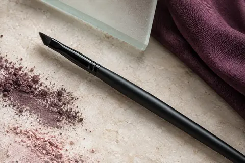 Pinceau eyeliner noir à fibres synthétiques denses et pointe fine posé sur une pierre claire.