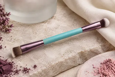 Pinceau de maquillage double embout au manche cyan, avec une tête plate et une tête angulaire.