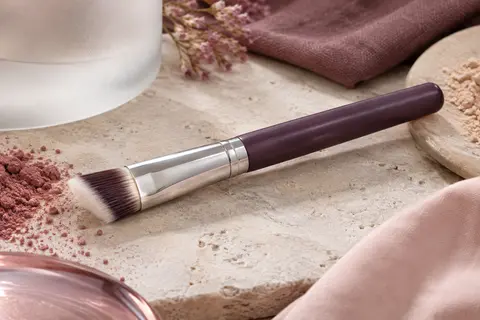 Pinceau correcteur compact à tête biseautée et fibres synthétiques posé sur une surface claire