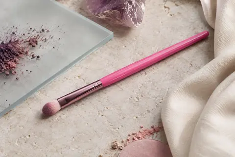 Pinceau correcteur rose vif à poils synthétiques posé sur une surface en pierre claire.
