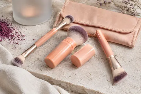 Trois pinceaux de maquillage Heymkgo couleur abricot et leur pochette souple disposés sur une pierre claire.