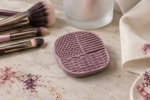 Disque de nettoyage pour pinceaux à maquillage posé sur une pierre claire, avec ses reliefs visibles