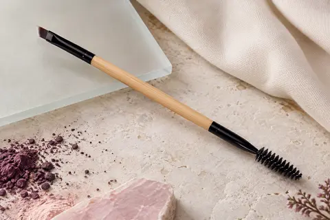 Pinceau noir à sourcils avec une tête biseautée et un spoolie, posé sur une surface claire.