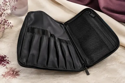 Trousse noire pliable ouverte, avec pochettes de rangement pour pinceaux et compartiments pour maquillage.