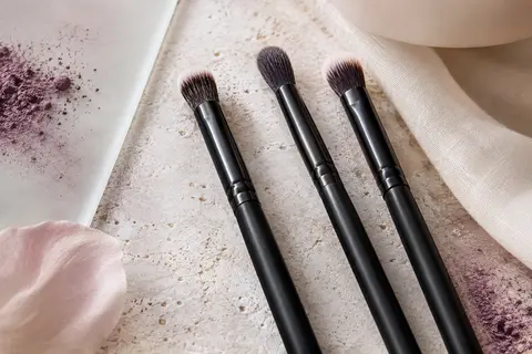 Trois pinceaux noirs pour les yeux, aux poils synthétiques, disposés sur une pierre claire.