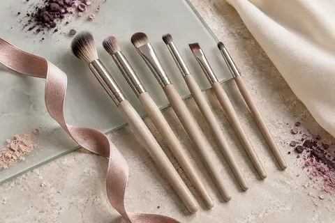 Six pinceaux pour les yeux et un ruban de maquillage disposés sur une surface claire.
