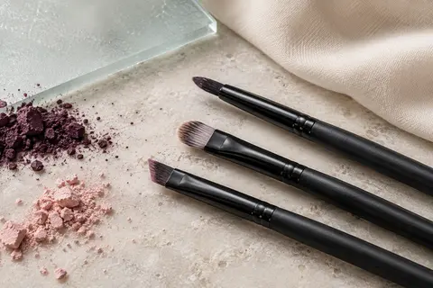 Trois pinceaux pour les yeux à manches noirs et têtes fines posés sur une pierre claire.