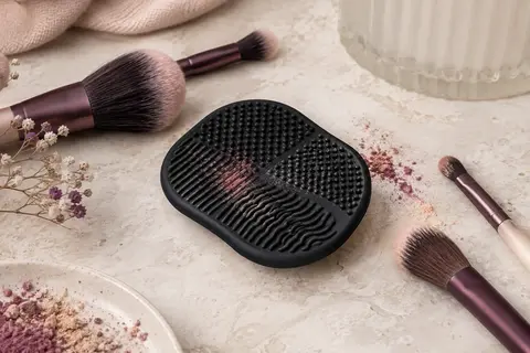 Tapis Color Switch noir en silicone texturé posé près de pinceaux de maquillage sur une pierre claire.