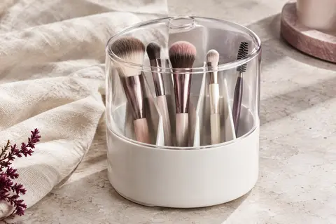 Organisateur blanc à couvercle transparent, compartimenté et rempli de pinceaux de maquillage