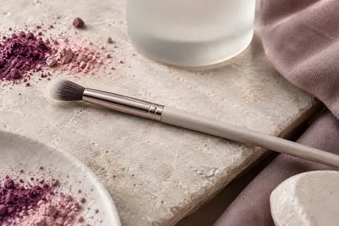 Pinceau estompeur à pointe longue et effilée posé sur une pierre claire près de pigments pour les yeux.