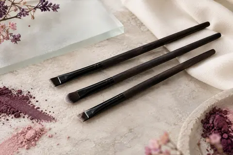 Trois pinceaux biseautés noirs pour eyeliner et sourcils posés sur une pierre claire.